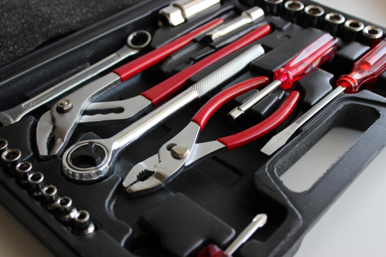Zbliżenie na czarną skrzynkę narzędziową zawierającą różne narzędzia, w tym szczypce, śrubokręty, klucz i wiele nasadek, wszystkie starannie ułożone z widocznymi czerwonymi i srebrnymi uchwytami.